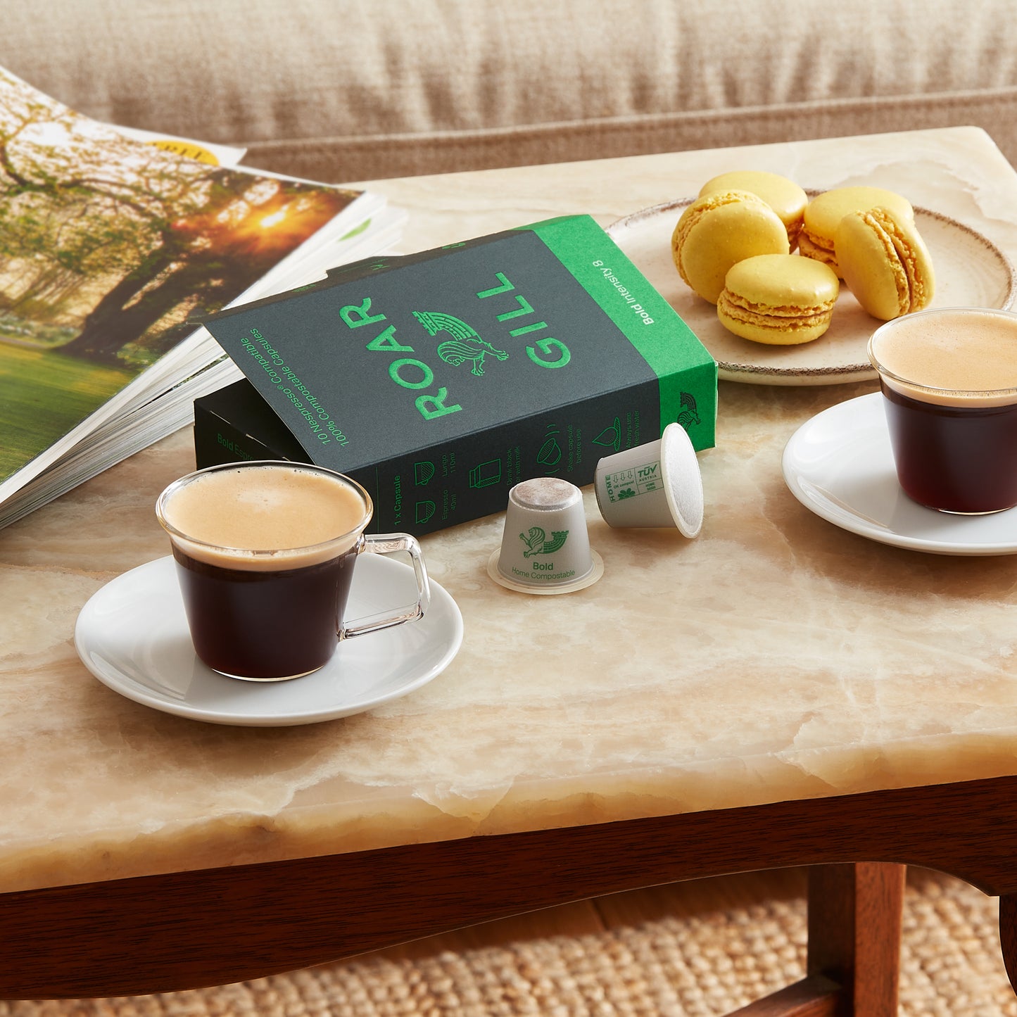 Bold coffee pods next to two poured espressos. Sat on coffee table with magazine and macarons.